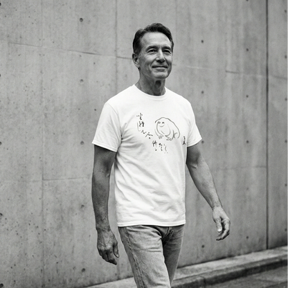 Man wearing a white t-shirt with a graphic design against a concrete wall.
