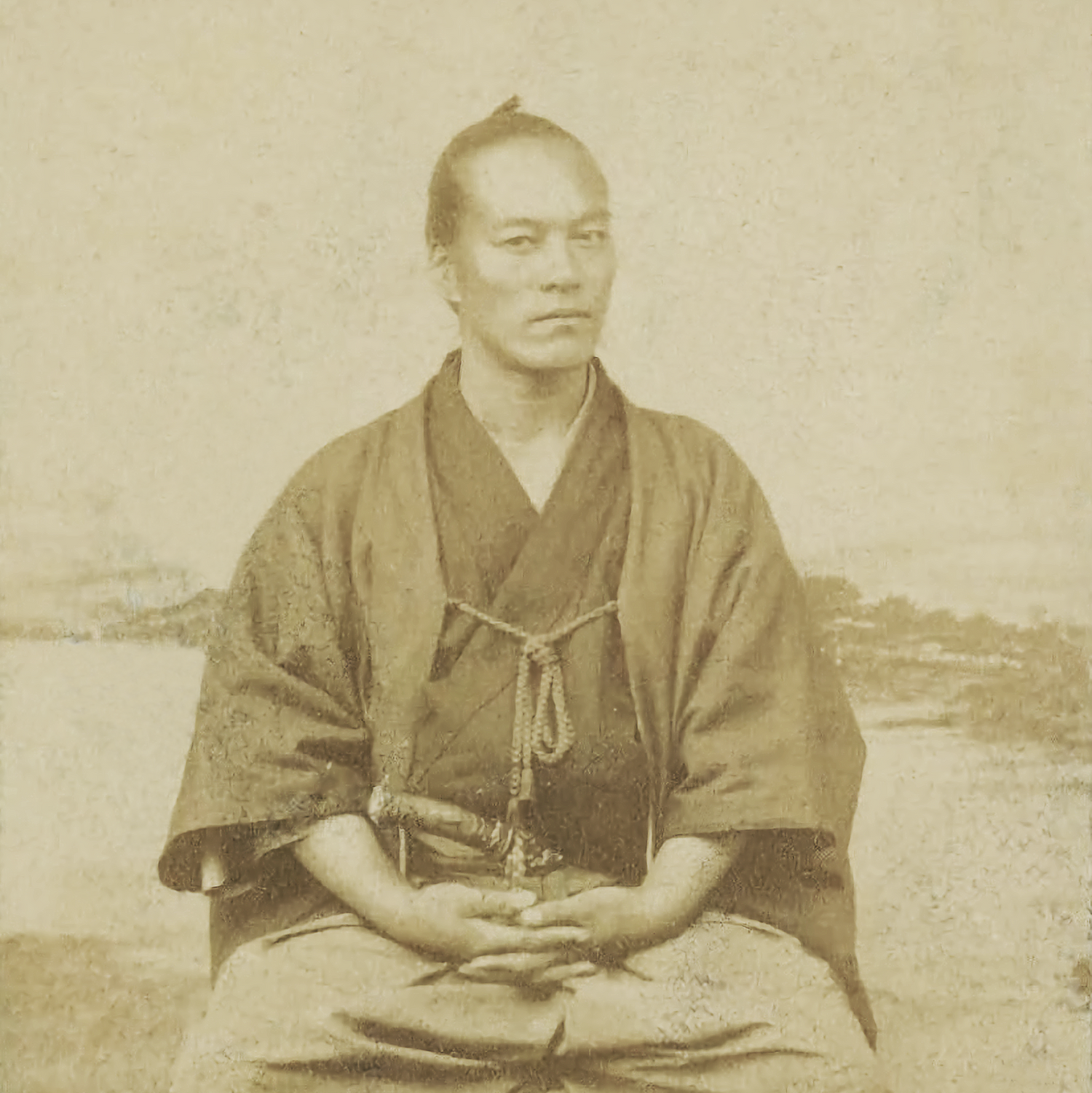 Vintage photograph of a person in traditional attire sitting on a stone surface.